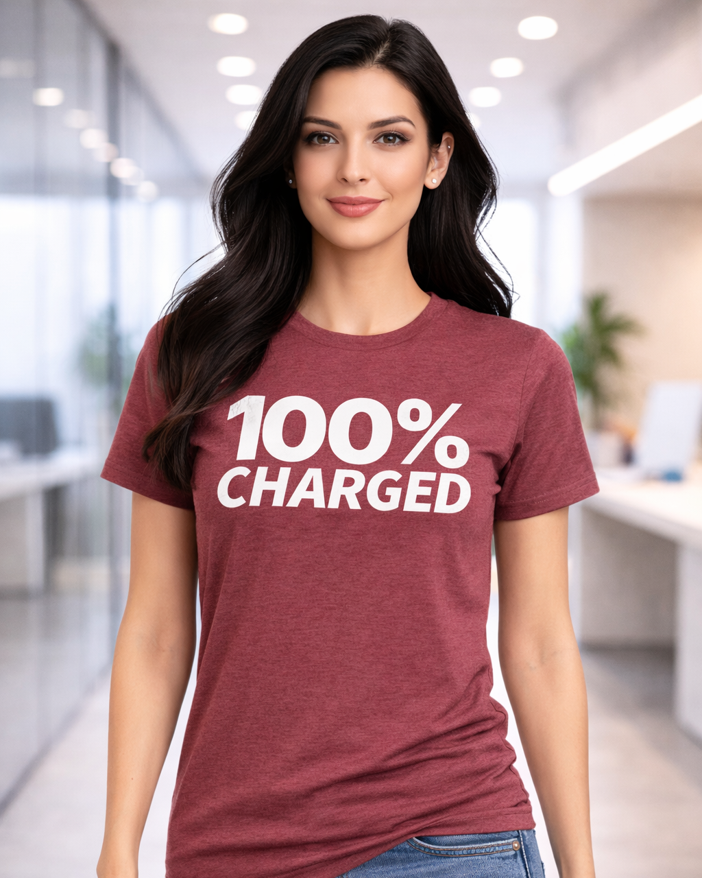Woman wearing a maroon t-shirt with '100% Charged' text in an office setting