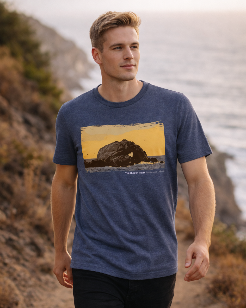 Man wearing a blue t-shirt with a nature graphic, standing on a trail with mountains in the background.