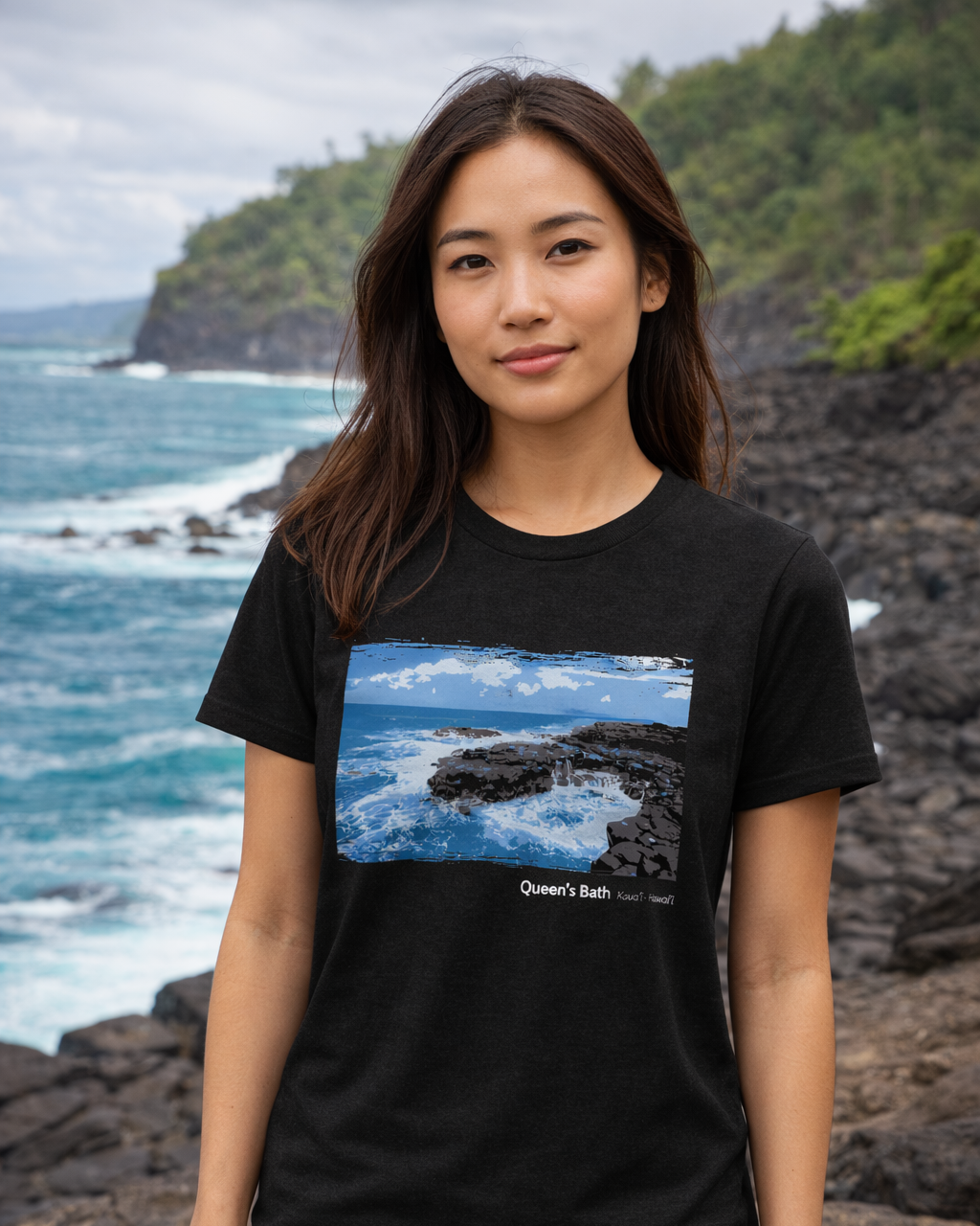 Woman wearing a black t-shirt with a scenic design, standing on a rocky beach.
