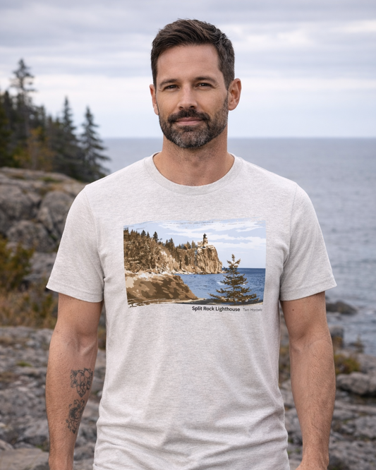 Man wearing a t-shirt with a scenic design of a lighthouse, standing outdoors by a body of water.