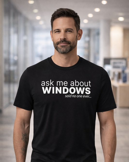 Man wearing a black t-shirt with 'ask me about WINDOWS said no one ever' text in an office setting.