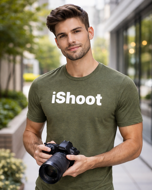 Man wearing a green t-shirt with 'iShoot' holding a camera outdoors.