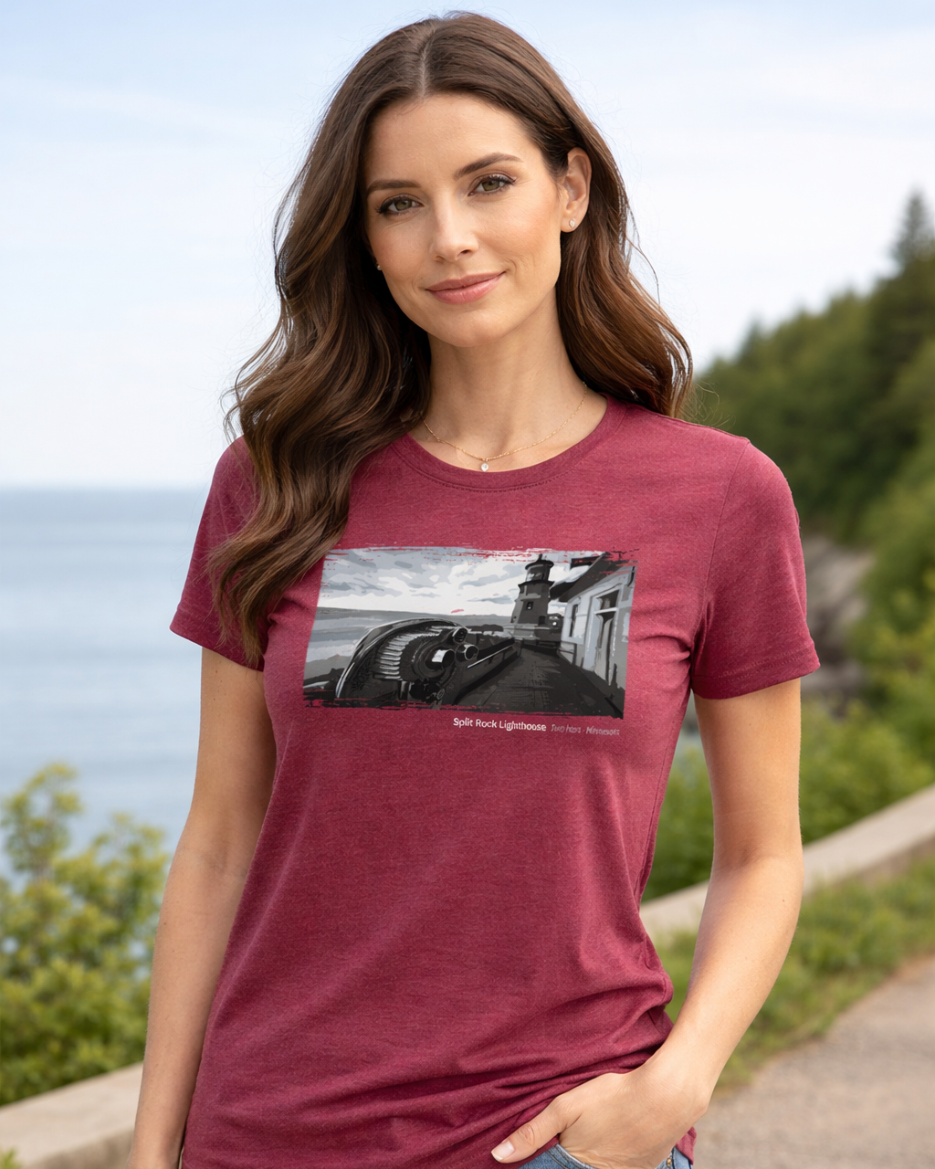 Woman wearing a maroon t-shirt with a graphic design, standing outdoors with greenery and water in the background.