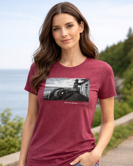 Woman wearing a maroon t-shirt with a graphic design, standing outdoors with greenery and water in the background.