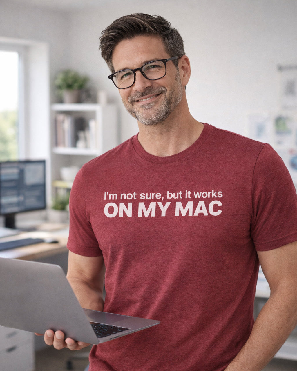 Man wearing a red t-shirt with text, holding a laptop in an office setting